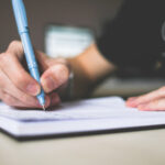 person-holding-blue-ballpoint-pen-writing-in-notebook-210661