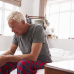 Senior Man Sitting On Bed At Home Suffering From Depression