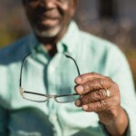 Mid section of senior African-American man holding spectacle in the park of nursing home